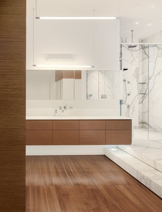 a contemporary bathroom with a wooden floor, a white marble shower space, a wooden vanity and a large mirror is bold and cool