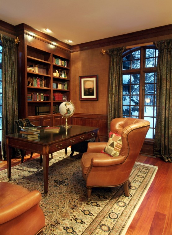 a vintage home office with rich stained furniture, leather chairs, printed curtains, a rug and fabric covered walls