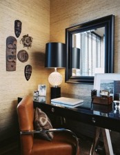 a refined home office with a black desk and a mirror in a black frame, masks for decor and an amber leather chair