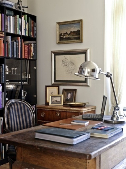 an eclectic home office with a modern bookcase, a rich stained desk, artworks and elegant metal lamps