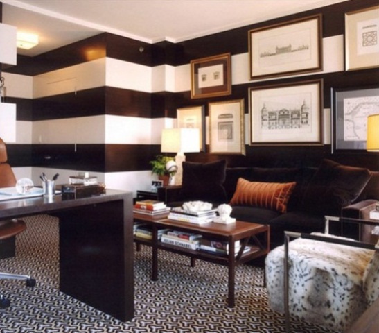 a modern home office with striped contrasting walls, a dark stained desk and a dark sofa plus rust and amber accents