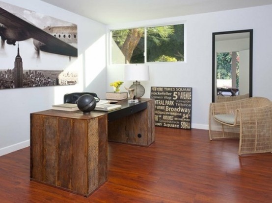 a unique home office with a reclaimed wood desk, a rattan chair and lots of unusual artworks