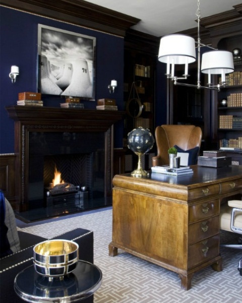 an elegant vintage-inspired masculine home office with navy walls, dark bookcases, a light stained desk and a leather chair