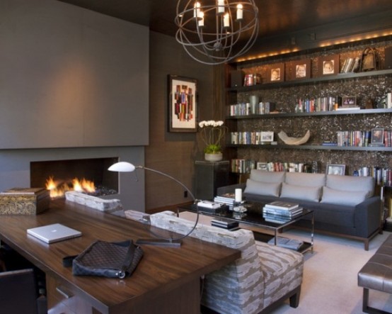 a moody home office with a concrete fireplace, a shiny wlal with open shelves, a rich stained wooden desk, catchy lamps and upholstered furniture