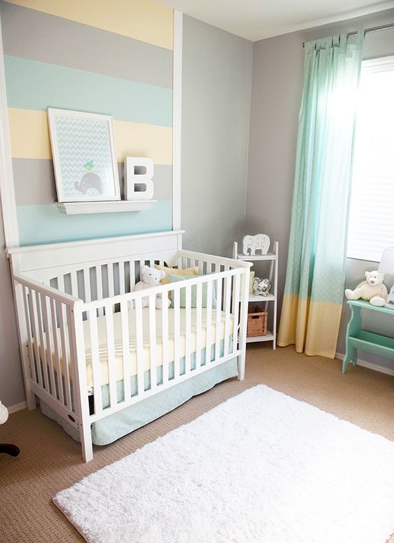 a pastel nursery with grey walls, white and mint colored furniture, pastel bedding and a printed rug plus a striped accent wall