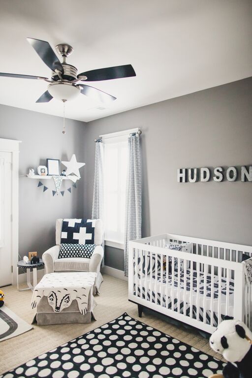 a monochromatic nursery with grey walls and white furniture, black and white textiles and a rug, a wall mounted shelf and a name over the bed