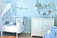 a dreamy light blue nursery with vintage white furniture, a grey chair with pillows, a rug and a wall-mounted shelf plus a lovely crystal chandelier