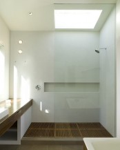 a white laconic bathroom with sleek walls, a window and a skylight, a wooden vanity and a shower with a wooden floor