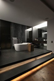 a minimalist moody bathroom with dark walls, a black floor, built-in lights, a stone accent walls, white appliances and a dark floating vanity