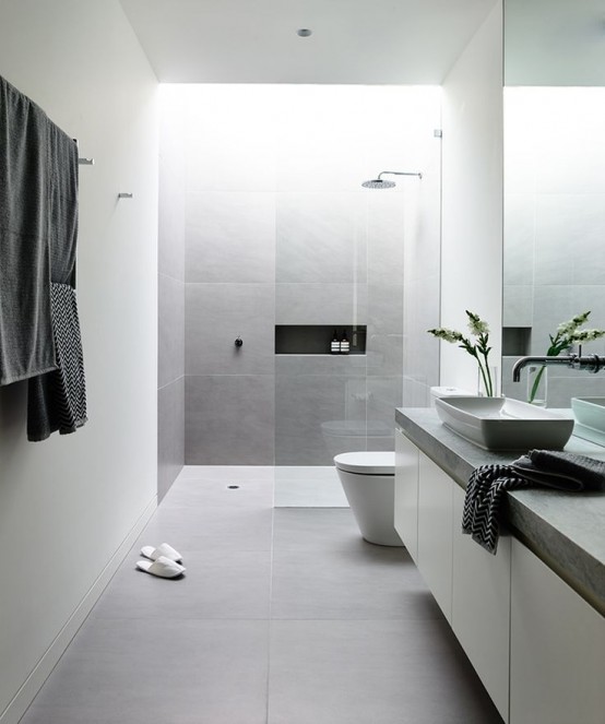 a minimalist grey and white bathroom with large scale tiles, a long vanity with a concrete countertop and a skylight over the shower