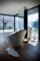a chic glass enclosed minimalist bathroom with a wooden floor, white free-standing appliances and a mirror pillar