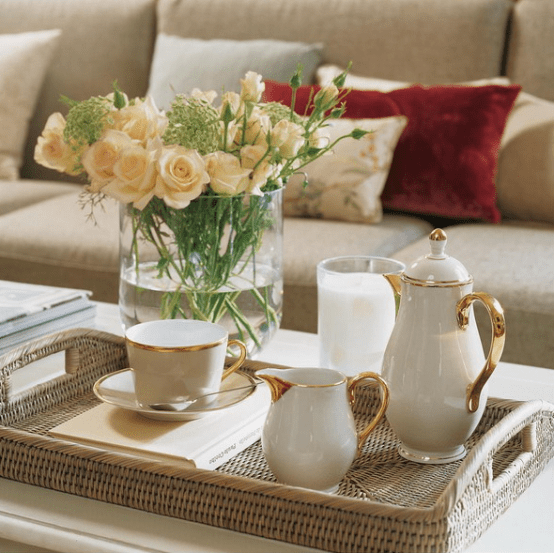 a white coffee table with a tray with elegant vintage coffeeware, a candle and a fresh bloom arrangement