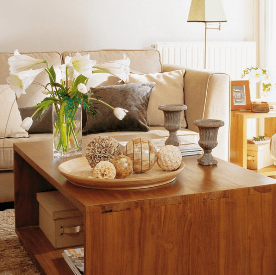 a sleek wooden coffee table with vintage urns, a floral arrangement, boxes and magazines