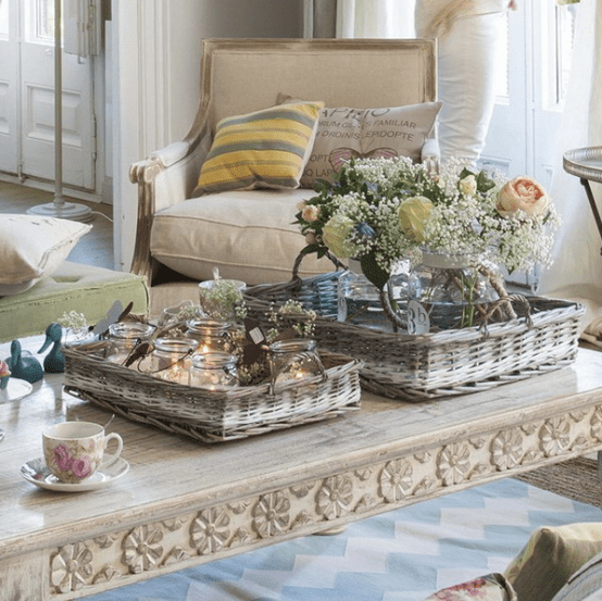 a carved rustic coffee table with baskets, candles in jars and fresh blooms in a vase