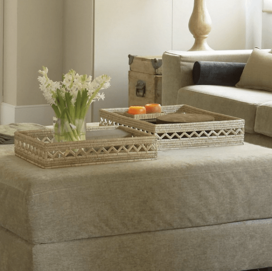 an upholstered ottoman that doubles as a coffee table and features two woven trays and fresh blooms and candles