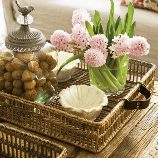 a rustic wooden coffee table with a woven tray, some pink blooms and a jar with nuts for decor