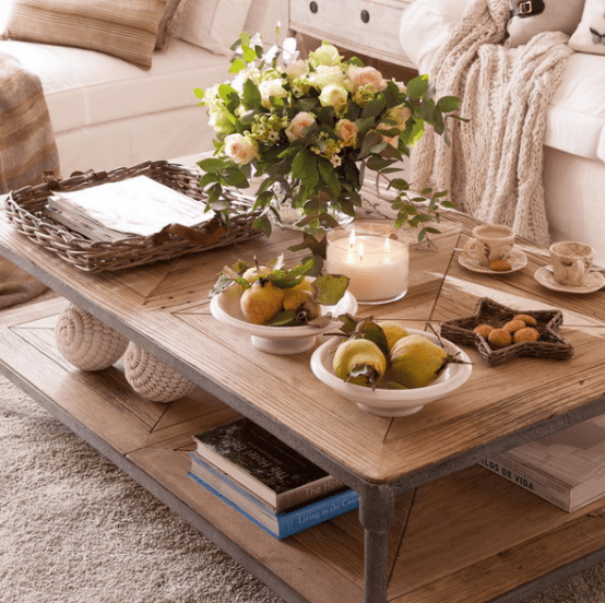 a rustic two tier coffee table with books, fruits, a fresh floral arrangement and a large candle