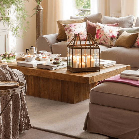 a rustic wooden coffee table with a large candle lantern, some vintage teacups, books and fresh blooms