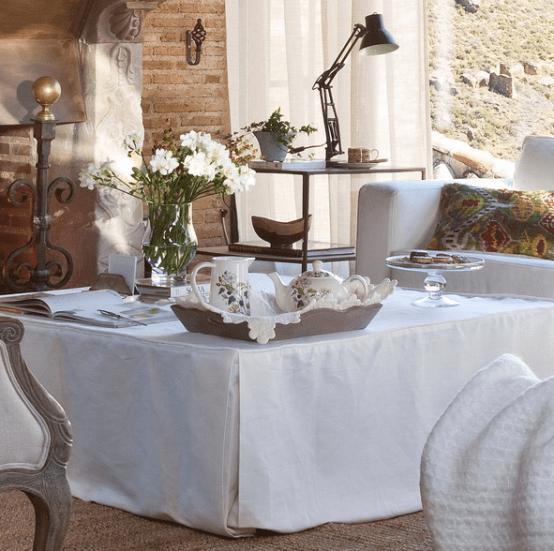 a large coffee table with a white tablecloth, a tray with teaware and some fresh blooms for a cute look