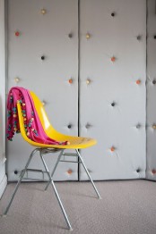 upholstered grey walls with colorful decorative nails make the space ultra-modern and playful