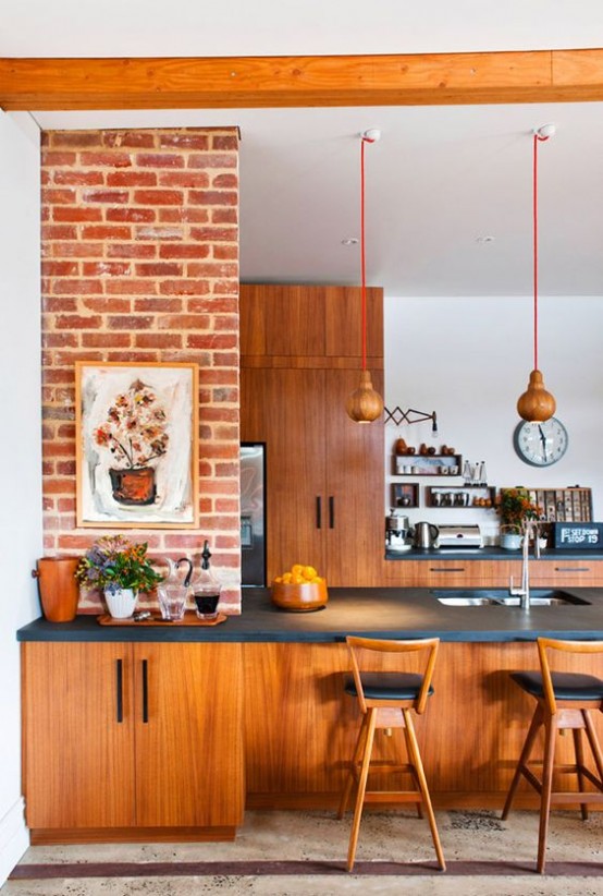 a bright mid-century modern kitchen with reddish furniture, pendant lamps, black countertops and artworks