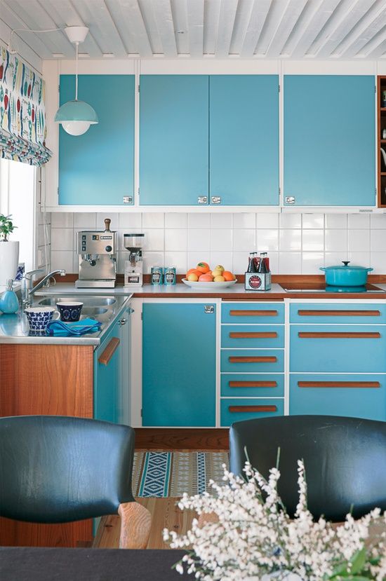 a bright turquoise and white mid-century modern kitchen with wooden handles, a white tile backsplash plus leather chairs