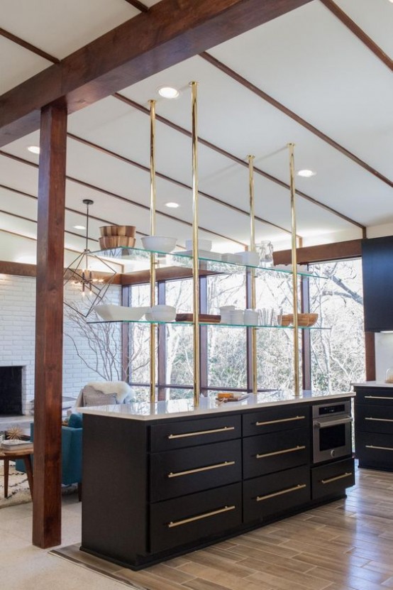 an oversized black kitchen island with gold handles and glass shelves over the island