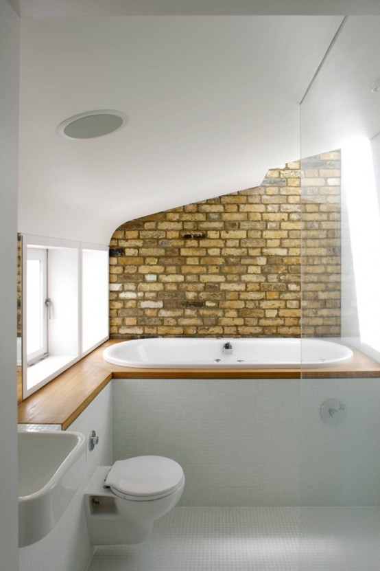 a laconic bathroom with white tiles, a built-in bathtub, a brick accent wall, a sink and toilet