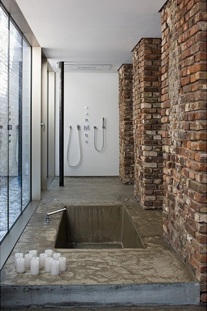a minimalist bathroom with brick walls, a built-in tub or shower space of concrete and lots of candles