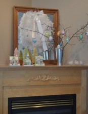 a pastel Easter mantel with an Easter tree and eggs hanging on it, a feather wreath and eggs hanging down
