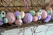 a colorful Easter mantel with fake eggs and yarn balls, with branches and a bird house