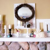 a bright Easter mantel with fake bunnies, colorufl eggs, a wreath with a bird and candles