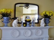 a bright Easter mantel with fake bunnies, yellow daffodils in blue and white pots and candle holders