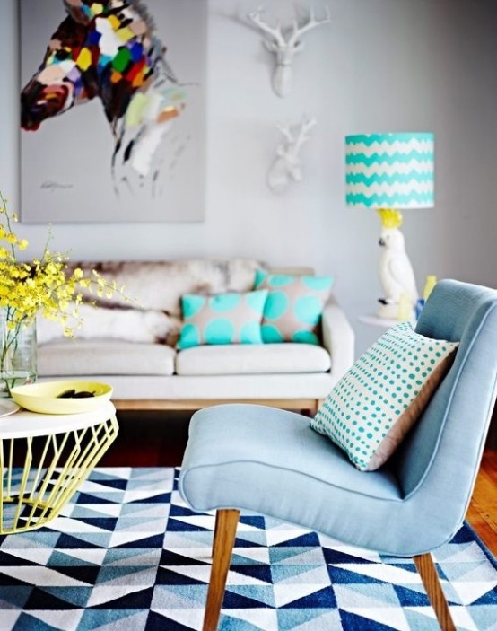 a bright living room with a neutral sofa, bright printed pillows, a bold geometric rug, a light blue chair and a coffee table with neon yellow legs and a bright table lamp
