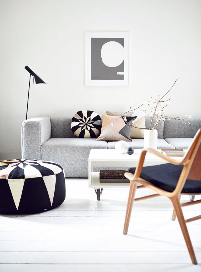 a dreamy Scandinavian living room with a grey sofa, pastel and geometric pillows and a pouf, a wihte coffee table on casters and a navy stained chair is amazing