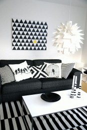 a black and white living room with a black sofa, a striped rug, a white coffee table, a geometric artwork and a wihte paper pendant lamp plus geometric pillows