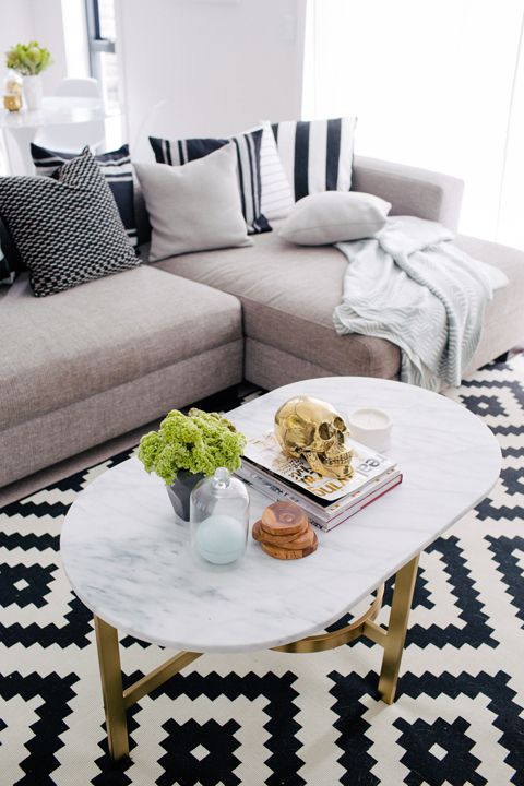 a Scandinavian sitting space with a grey sofa, neutral and striped pillows, a geometric black and white chair, an oval table with pretty decor