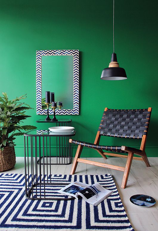 a stylish and bold living room with emerald walls, a couple of metal side tables, a black leather chair and a lamp, a black and white geometric rug tables,