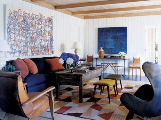 a bright living room with a colorful geometric rug, a navy sofa anda chair, a bright artwork and leather chairs or stools