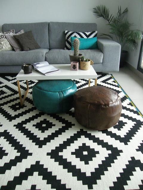a stylish modern living room with a grey sofa, geometric and bright pillows, geo printed rug and leather poufs plus a potted plant