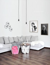 a serene Scandinavian living room with a grey sectional, geometric base coffee tables, pendant bulbs, a geometric sconce with bulbs on the wall