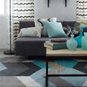a mid-century modern living room with a chevron printed rug, a coffee table with blue glass bottles, a grey sofa with printed pillows and chevron print curtains