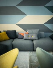 a muted color living room with a cool geo accent wall, a grey sofa, yellow and grey chairs is a chic idea
