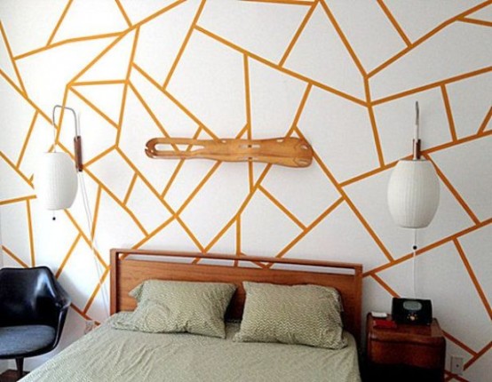 a modern bedroom with an orange and white geo print wall that takes over the whole space, a stained side table and a black chair