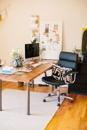 a pretty home office with an industrial desk of wood and metal, a black leather chair, some memo boards and a tassel garland