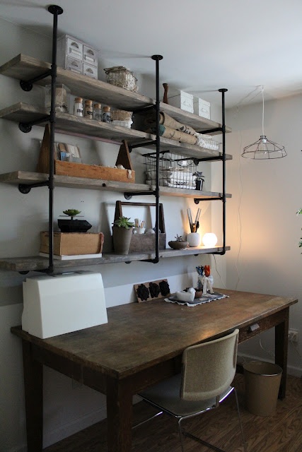 an industrial shelving unit of pipes and wood for storage, a shabby wooden desk to match it and for comfortable working