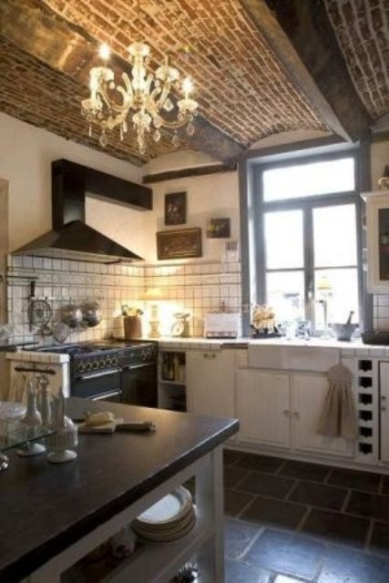 a red brick ceiling with beams is highlighted with a crystal chandelier and contrasts the neutral kitchen