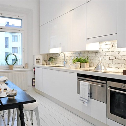 sleek white cabinets are complemented with a white brick backsplash and a white wooden floor that add texture to the space