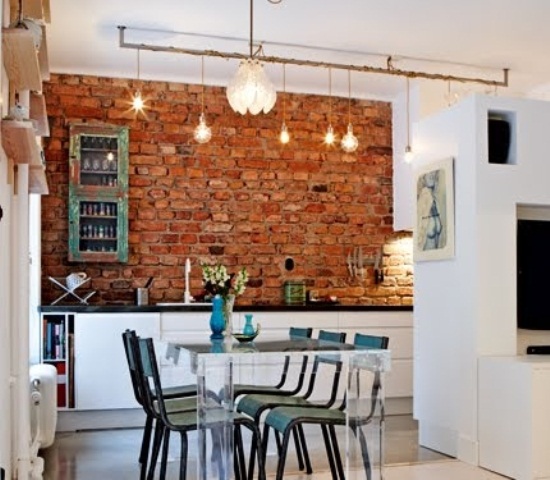 a red brick statement wall stands out in a sleek white kitchen and adds color and texture to the space