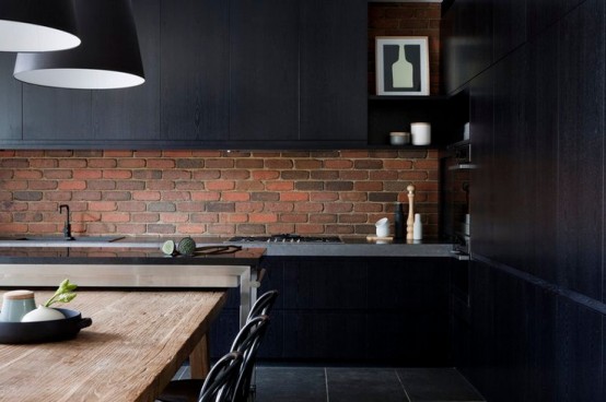 a moody black kitchen with a red brick backsplash that enlivens the space and makes it bolder and cooler
